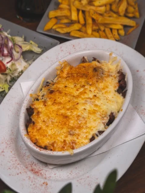 Mit Käse überbackenes Gericht mit Pommes und Salat bei Zaki’s